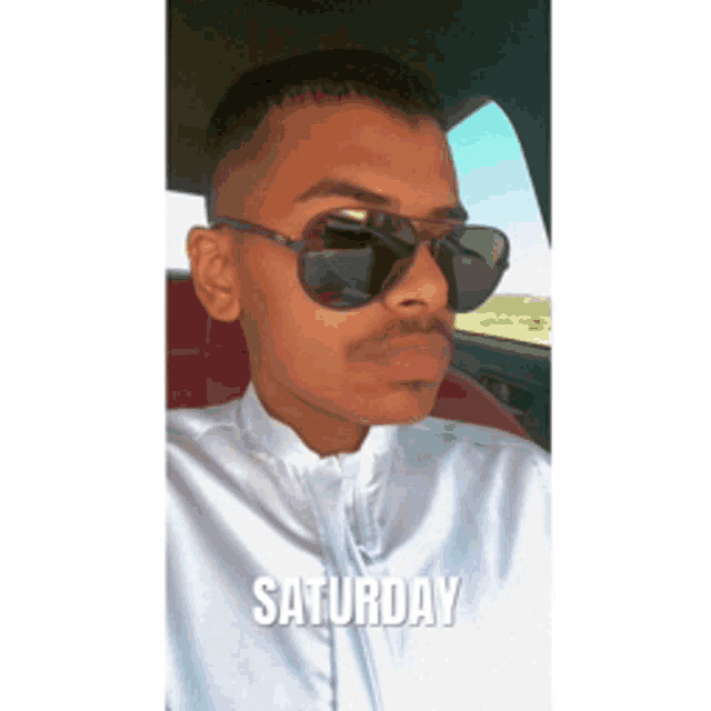 a man wearing sunglasses is sitting in a car with saturday written on the bottom