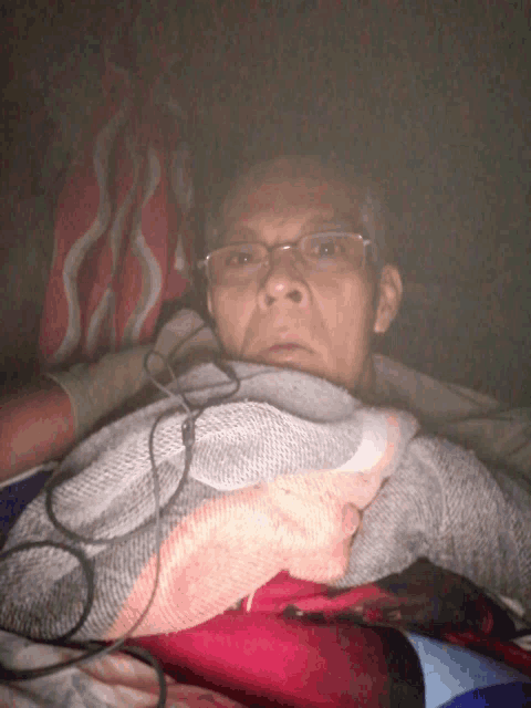 a man wearing glasses is laying in a bed with a blanket