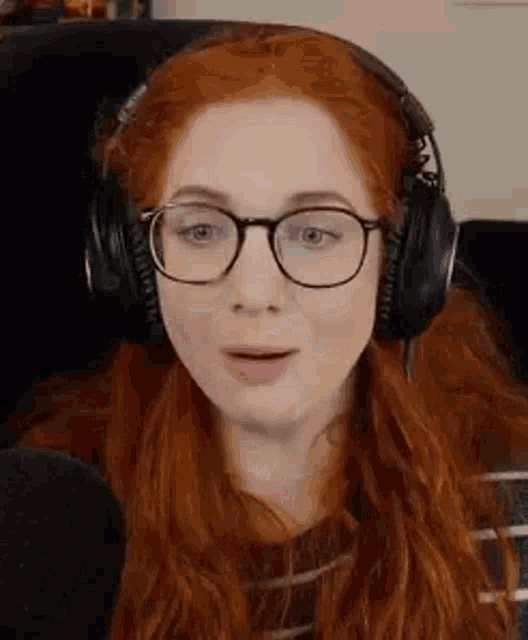 a woman with red hair is wearing headphones and glasses while sitting in front of a microphone .