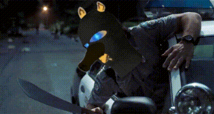 a police officer is standing next to a police car with a dog mask on his head .