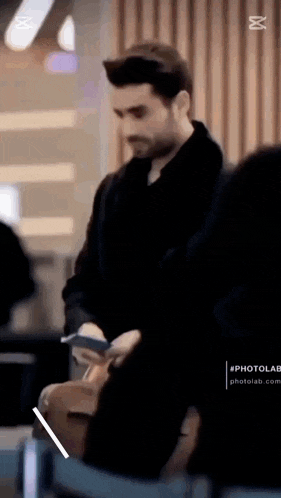 a man in a black coat is standing in an airport holding a suitcase .
