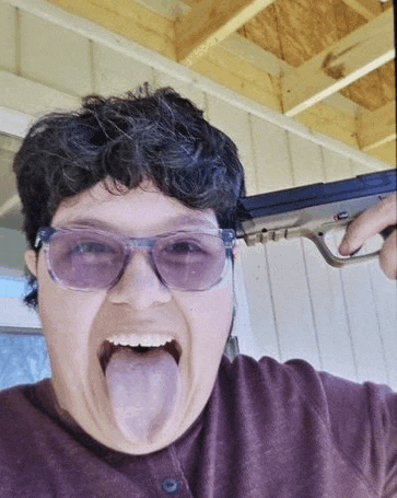 a woman wearing sunglasses is sticking her tongue out and holding a gun .