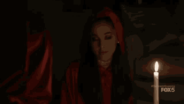 a woman in a red hood sits in front of a lit candle .