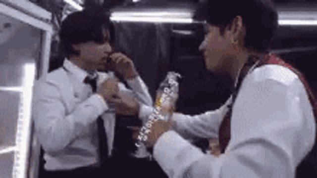 two men in suits and ties are standing next to each other . one of the men is holding a bottle of water .