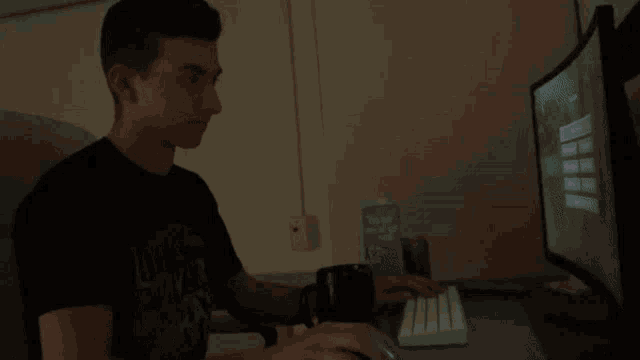 a man wearing a black shirt that says luck saver on it sits in front of a computer
