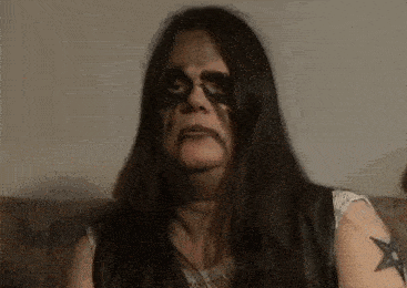 a woman with long black hair and a tattoo on her arm is sitting on a couch and looking at the camera .