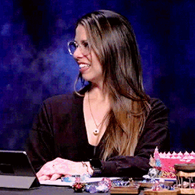 a woman wearing glasses sits at a table with a tablet