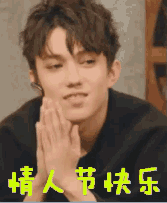 a young man with his hands folded in front of his face with chinese writing behind him