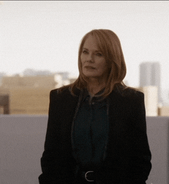a woman wearing a black jacket and a green shirt stands in front of a city skyline