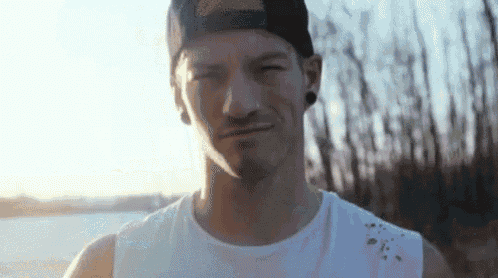 a man wearing a baseball cap and a white tank top is smiling .