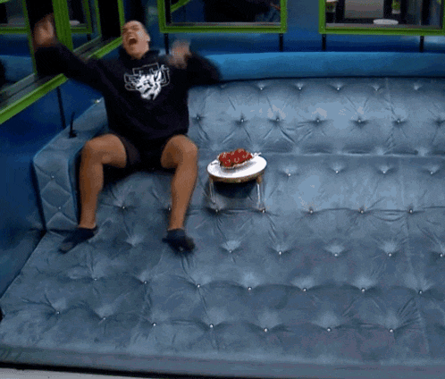 a man is sitting on a blue couch with a bowl of strawberries on a small table