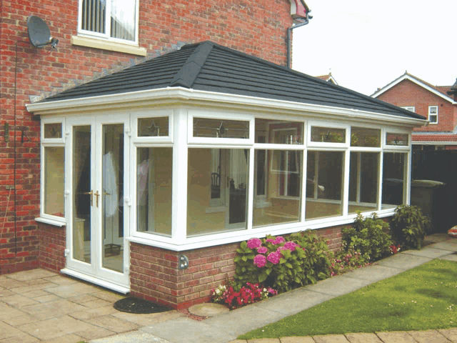 a brick house with a black roof and a white conservatory on the side