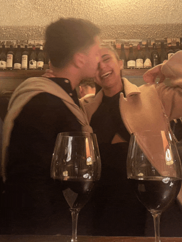 a man kisses a woman on the cheek in front of two glasses of red wine