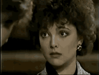 a woman with curly hair and earrings is looking at the camera in a close up of her face .