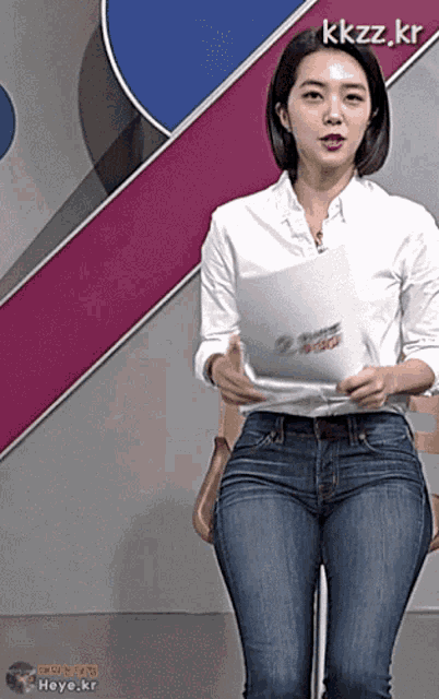 a woman wearing jeans and a white shirt is holding a piece of paper with kkzz.kr written on it