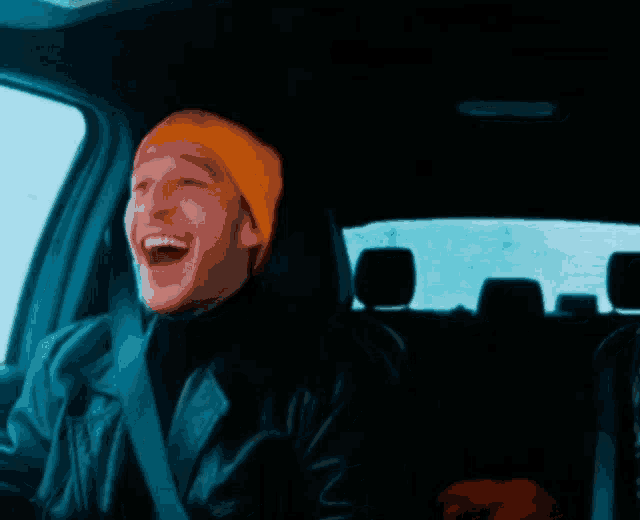 a man wearing a yellow hat is laughing while driving a car