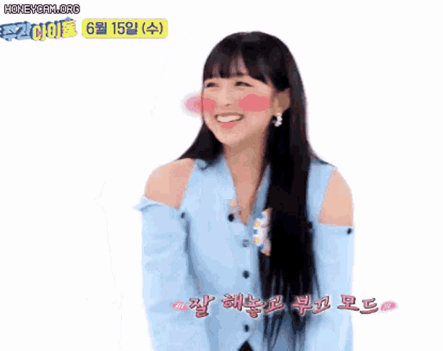 a girl with long hair and a blue cardigan is smiling with korean writing on her face .