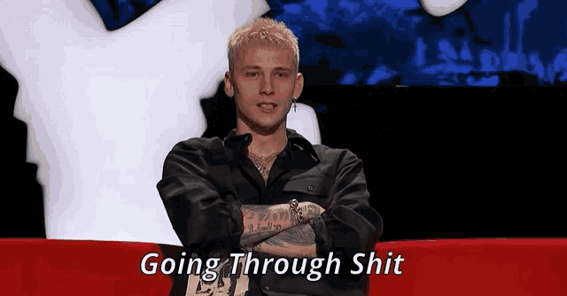 a man with his arms crossed is sitting on a red couch with the words going through shit above him