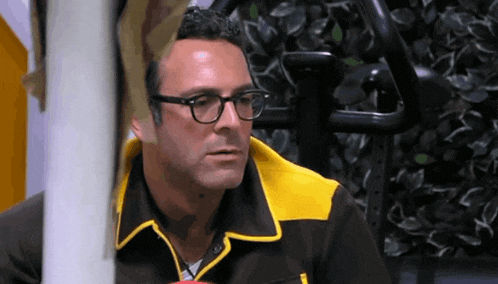 a man wearing glasses and a yellow jacket is looking at something