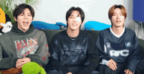 three young men are sitting on a couch and one of them is wearing a shirt that says rc