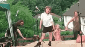 a group of people are standing on a stage holding hands and dancing in front of a microphone .