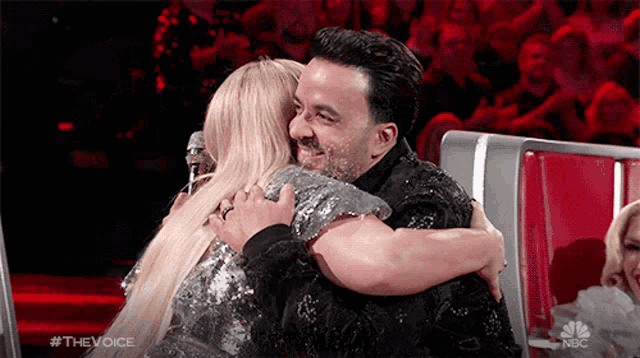 a man and a woman are hugging each other in front of a crowd on nbc 's the voice show .