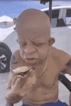 a bald man with a chain around his neck is eating a oyster