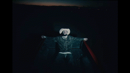 a man in a cowboy hat and robe is standing in the dark .