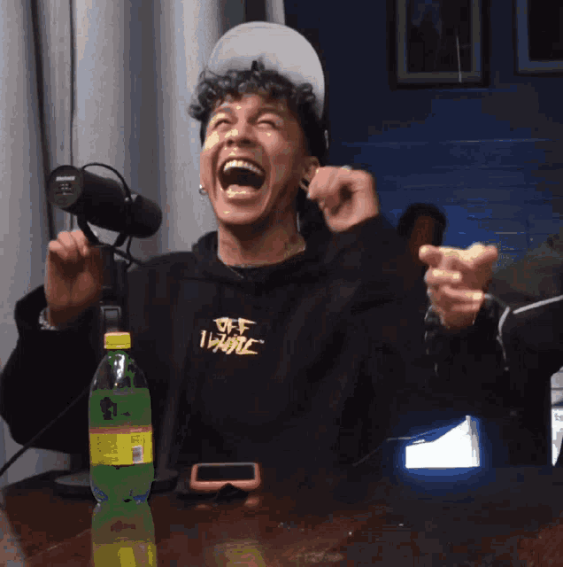 a man wearing a black hoodie that says off white is laughing in front of a shure microphone