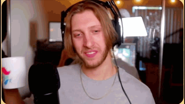 a man wearing headphones and a necklace is holding a cup in front of a microphone .