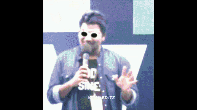 a man wearing sunglasses and a shirt that says no sins holds a microphone