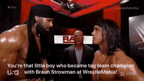 two wrestlers are standing next to each other in a room and one of them is talking to the other .