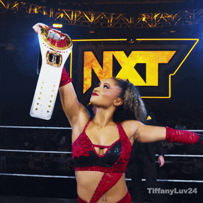a woman holding a wrestling belt in front of a nxt logo