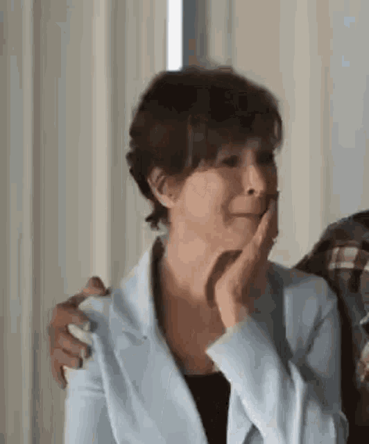 a woman in a blue jacket is sitting next to a man in a plaid shirt and covering her face with her hand .