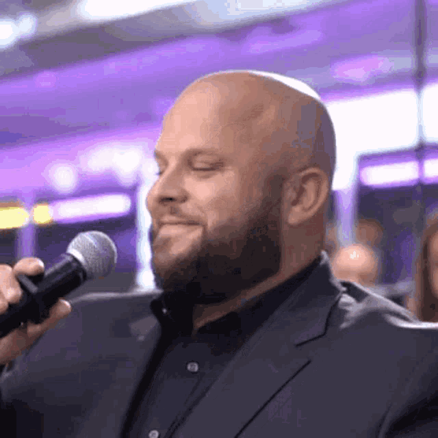a bald man with a beard is holding a microphone and smiling