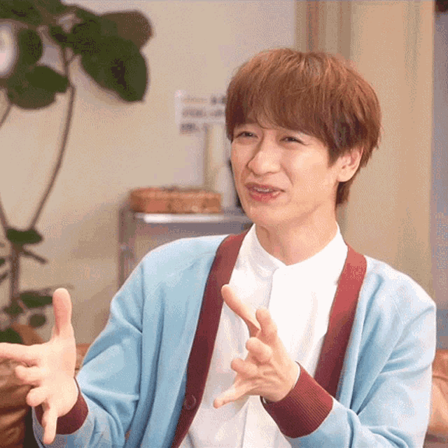 a man wearing a blue cardigan and a white shirt is making a gesture with his hands