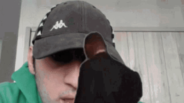 a man wearing a kappa hat is holding a pair of socks in front of his face
