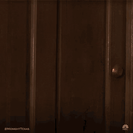 a woman is peeking out of a door and looking at the camera .