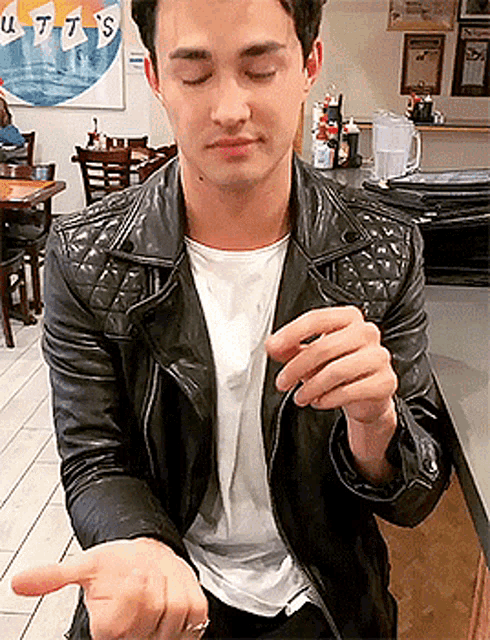 a man wearing a black leather jacket and a white shirt is sitting in front of a sign that says utta 's