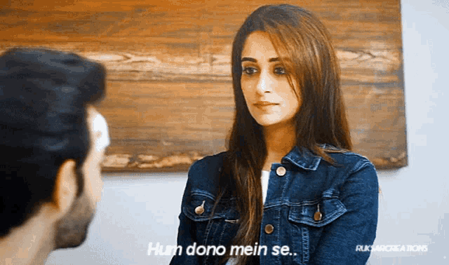a woman in a denim jacket is talking to a man and says hum dono mein se