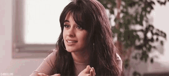 a woman with long hair and bangs is sitting at a table and smiling at the camera .