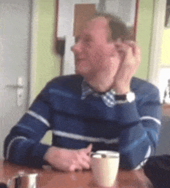 a man is sitting at a table with a cup of coffee and a cell phone .