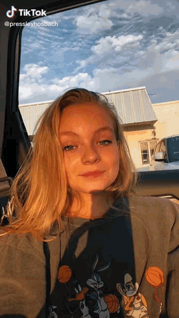 a young woman is sitting in the back seat of a car wearing a sweatshirt with bugs bunny on it .