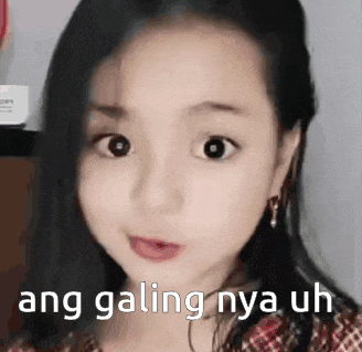 a little girl is making a funny face with the words ang galing nya uh written on her face .