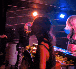 a woman in a red tank top is standing in front of a drum set in a dark room
