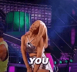 a woman in a silver top and shorts is dancing on a stage with the word you above her