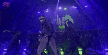 a man in a purple jacket is dancing on a stage in front of a sign that says " so "