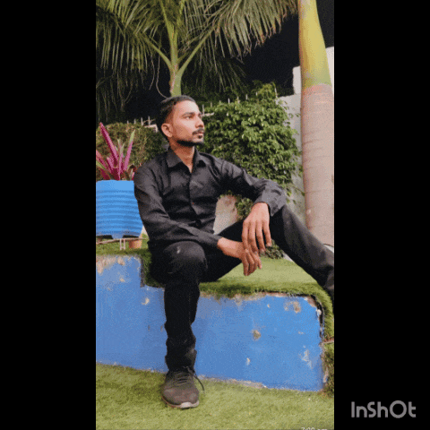 a man in a black shirt sits on a blue wall in front of a palm tree