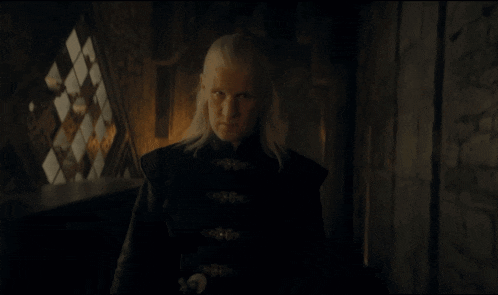 a man with long blonde hair stands in a dark room