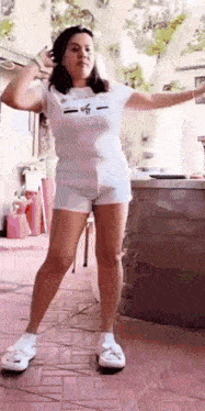 a woman in a white shirt and shorts is standing on a brick floor .